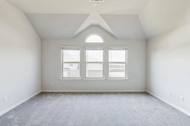 empty room with light colored carpet, vaulted ceiling, visible vents, and baseboards