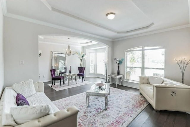 living room featuring an inviting chandelier, a tray ceiling, dark wood-style flooring, and ornamental molding