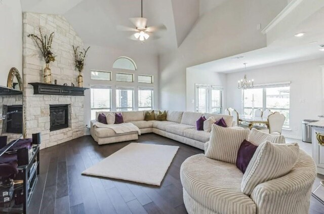 living area featuring high vaulted ceiling, dark wood-style flooring, a stone fireplace, and ceiling fan with notable chandelier