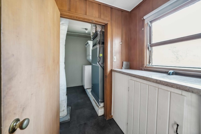 hall featuring stacked washer and dryer, wooden walls, and dark tile patterned flooring