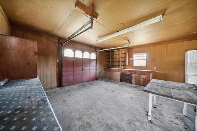 garage with stacked washer and clothes dryer and wooden walls