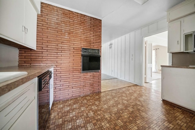 kitchen featuring white cabinets, brick wall, dishwashing machine, and oven