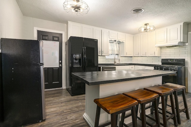 kitchen with a breakfast bar area, white cabinetry, a center island, black appliances, and decorative backsplash