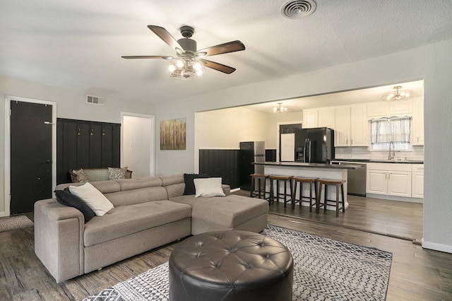 living room with sink, dark hardwood / wood-style floors, ceiling fan with notable chandelier, and a textured ceiling