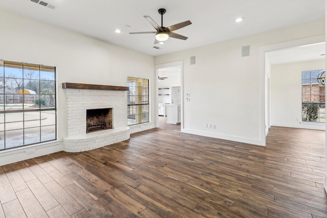 unfurnished living room featuring dark wood-type flooring, ceiling fan, and a brick fireplace