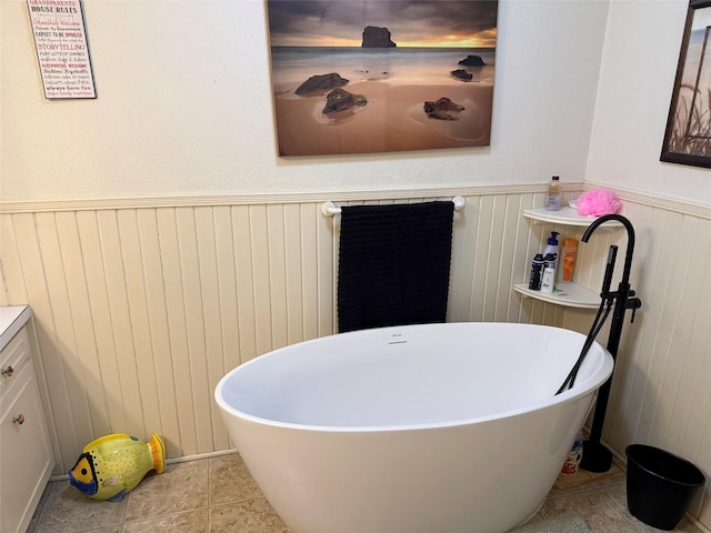 full bath with a wainscoted wall, vanity, a soaking tub, and tile patterned flooring