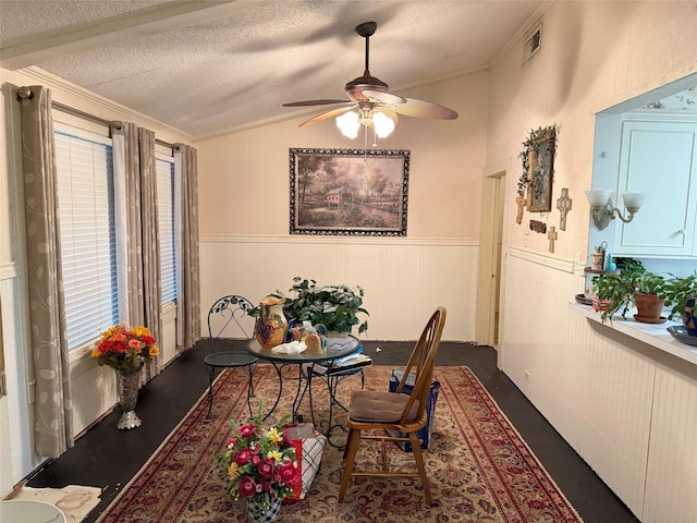 dining space with crown molding, a ceiling fan, a textured ceiling, vaulted ceiling, and wainscoting