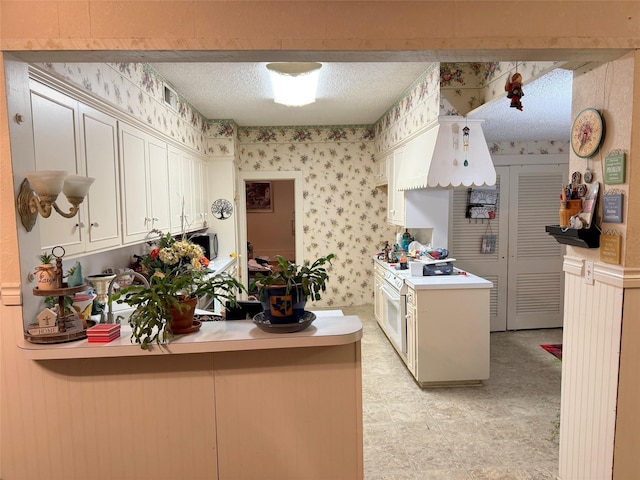 kitchen with light countertops, a peninsula, wallpapered walls, a textured ceiling, and cream cabinetry