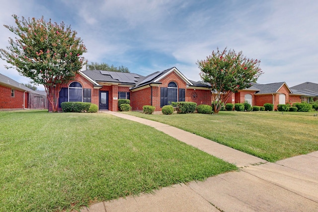 ranch-style house with brick siding, roof mounted solar panels, a front yard, and fence