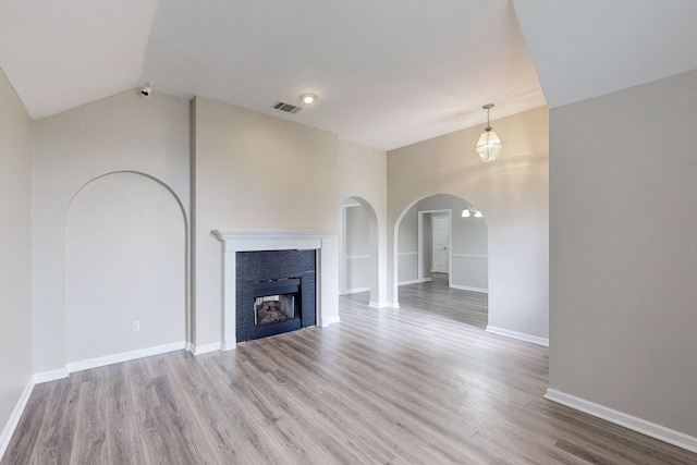 unfurnished living room with baseboards, visible vents, lofted ceiling, wood finished floors, and a fireplace