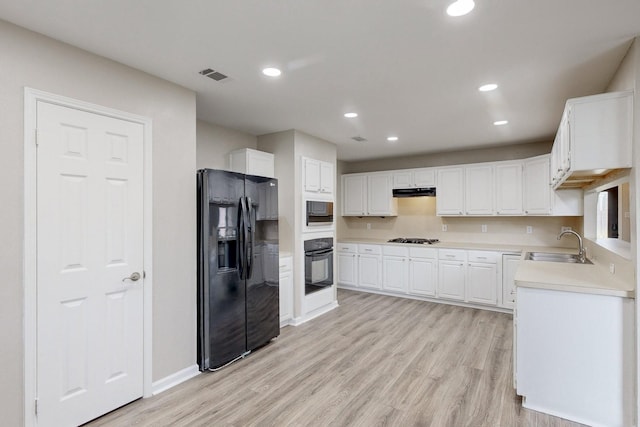 kitchen featuring visible vents, light wood finished floors, black appliances, a sink, and light countertops