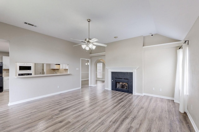 unfurnished living room featuring a tiled fireplace, light wood finished floors, lofted ceiling, and ceiling fan