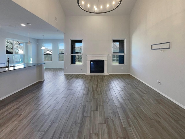 unfurnished living room with dark wood-type flooring, sink, an inviting chandelier, and a high ceiling