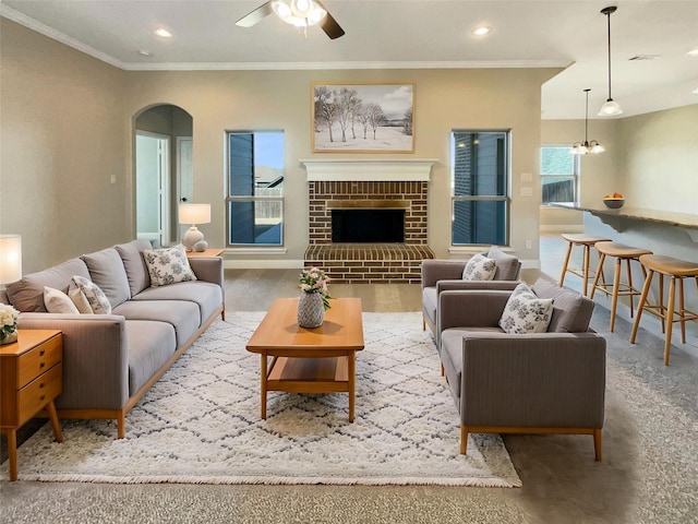 living room featuring hardwood / wood-style flooring, ornamental molding, ceiling fan with notable chandelier, and a fireplace