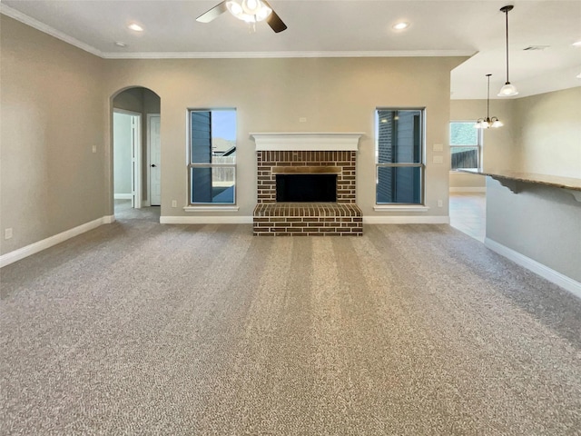 unfurnished living room featuring crown molding, ceiling fan with notable chandelier, carpet floors, and a brick fireplace