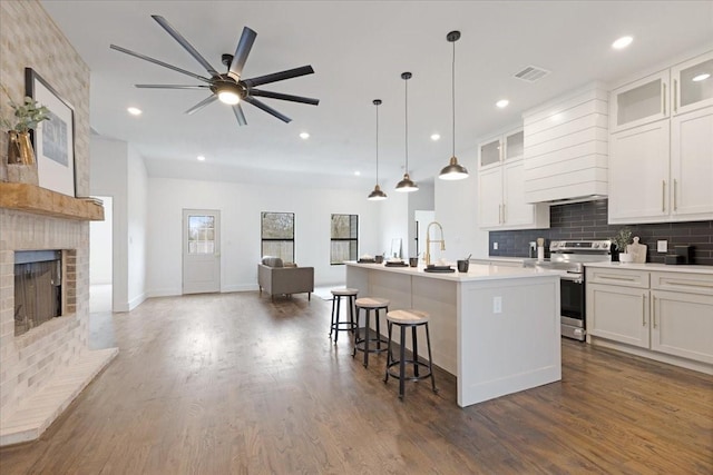 kitchen featuring electric stove, light countertops, glass insert cabinets, open floor plan, and an island with sink