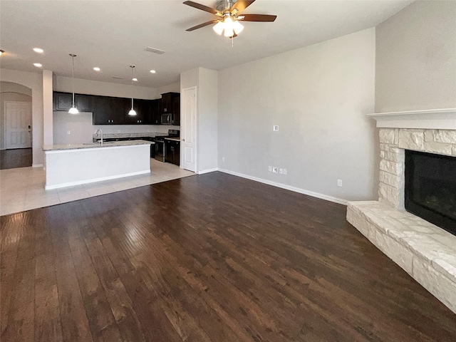 unfurnished living room featuring dark hardwood / wood-style flooring, sink, a fireplace, and ceiling fan