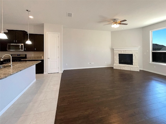 unfurnished living room featuring hardwood / wood-style flooring, a stone fireplace, sink, and ceiling fan