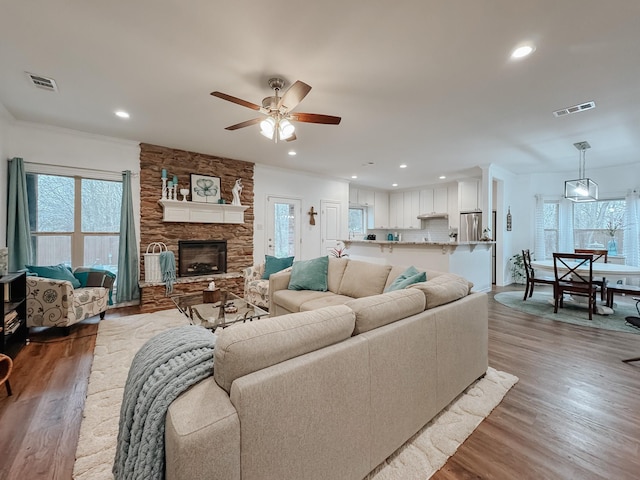 living room with a stone fireplace, light hardwood / wood-style flooring, and ceiling fan