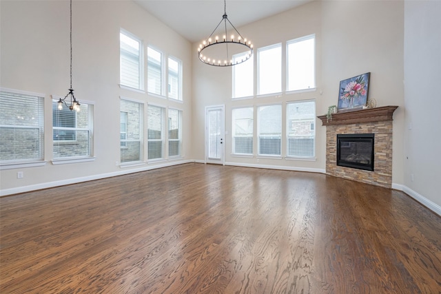 unfurnished living room featuring a notable chandelier, a high ceiling, dark wood-type flooring, a stone fireplace, and baseboards