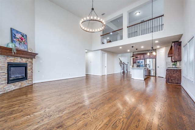 unfurnished living room featuring a chandelier, dark wood-type flooring, a fireplace, and baseboards