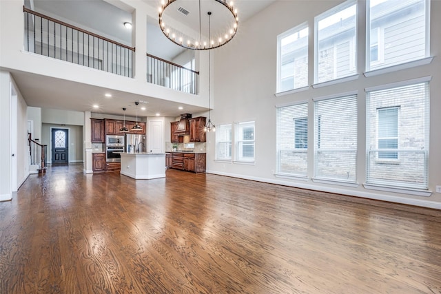 unfurnished living room featuring dark wood finished floors, visible vents, a chandelier, baseboards, and stairs