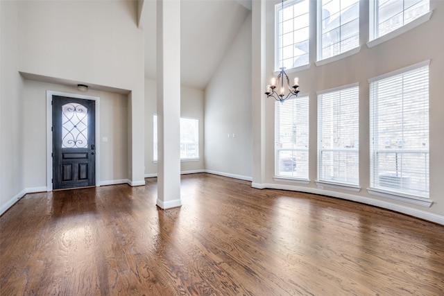 foyer featuring decorative columns, a chandelier, wood finished floors, high vaulted ceiling, and baseboards