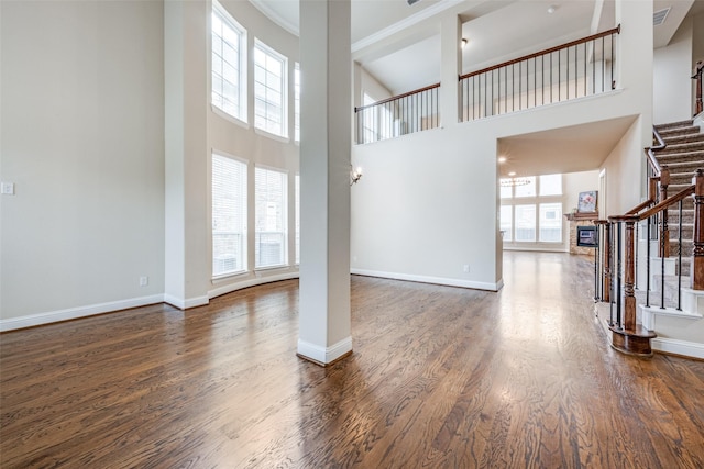 unfurnished living room with a wealth of natural light, dark wood finished floors, and stairway