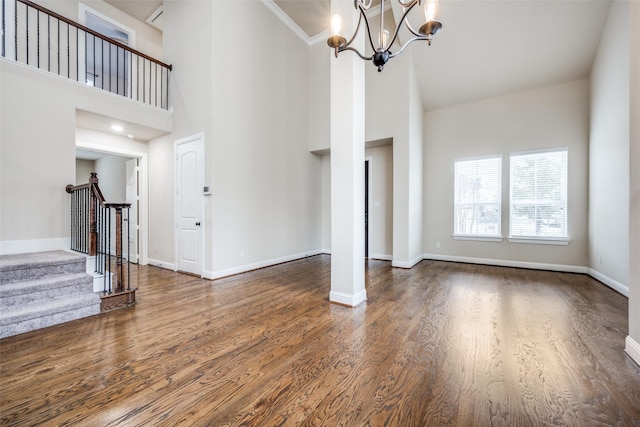 unfurnished living room with a high ceiling, an inviting chandelier, wood finished floors, baseboards, and stairs