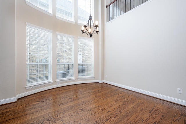 spare room with baseboards, dark wood finished floors, and a notable chandelier