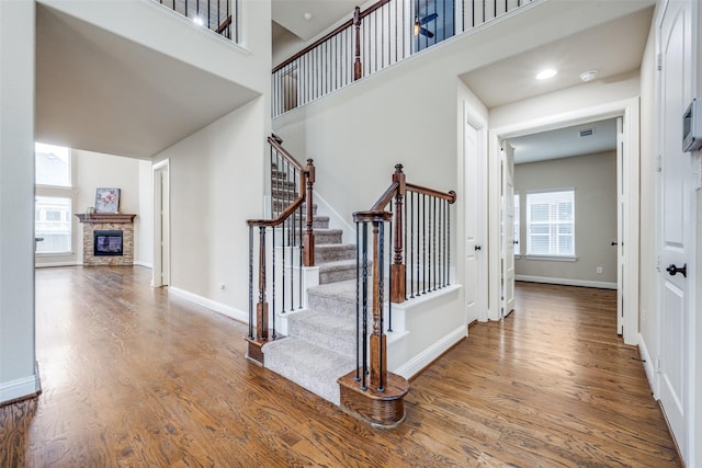 staircase with a high ceiling, a fireplace, wood finished floors, and baseboards