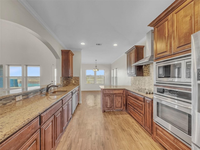 kitchen with sink, appliances with stainless steel finishes, decorative light fixtures, kitchen peninsula, and wall chimney exhaust hood