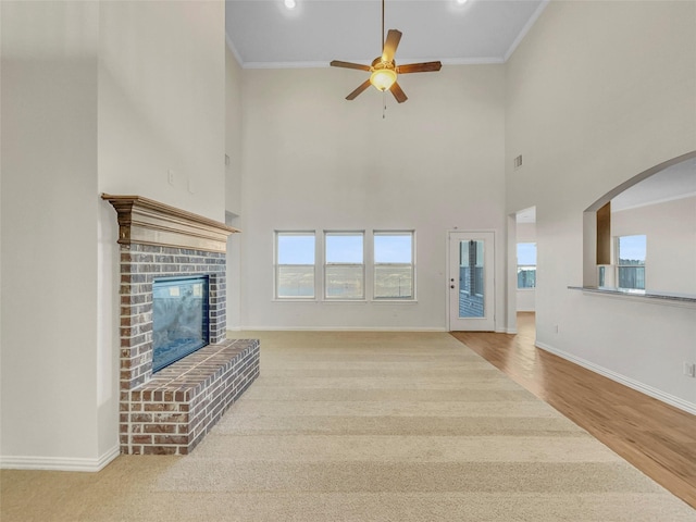 unfurnished living room with ornamental molding, a brick fireplace, ceiling fan, and light wood-type flooring