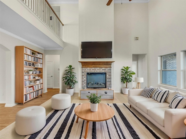 living room with crown molding, a brick fireplace, hardwood / wood-style flooring, and a towering ceiling