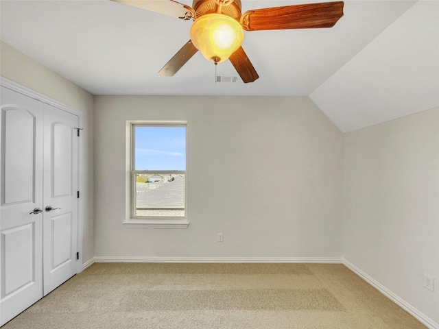 unfurnished bedroom featuring ceiling fan, light colored carpet, vaulted ceiling, and a closet