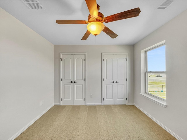 unfurnished bedroom with light carpet, ceiling fan, and multiple closets