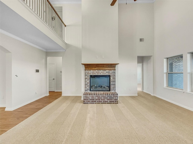 unfurnished living room featuring a high ceiling, light colored carpet, ceiling fan, crown molding, and a brick fireplace