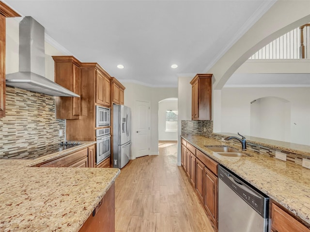 kitchen with wall chimney range hood, stainless steel appliances, light hardwood / wood-style floors, and light stone countertops