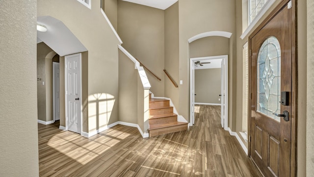 foyer with hardwood / wood-style flooring, a towering ceiling, and ceiling fan