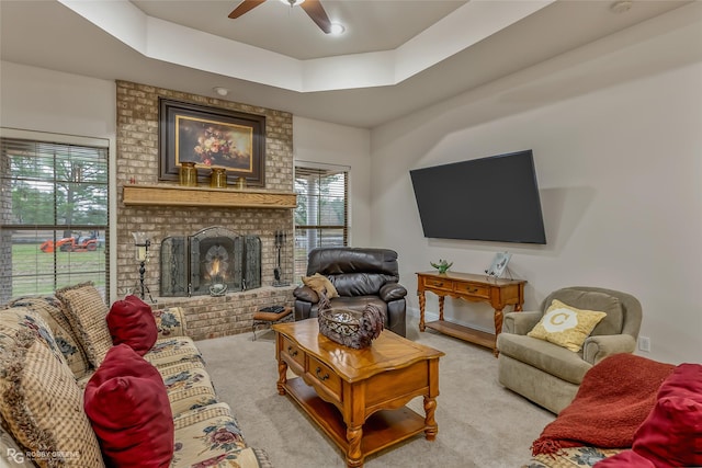 carpeted living room featuring ceiling fan, a tray ceiling, and a brick fireplace