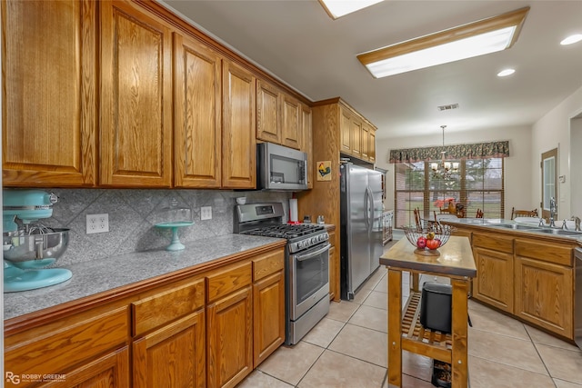 kitchen featuring sink, light tile patterned floors, appliances with stainless steel finishes, hanging light fixtures, and decorative backsplash