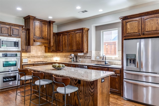 kitchen featuring sink, appliances with stainless steel finishes, a center island, ornamental molding, and light stone countertops