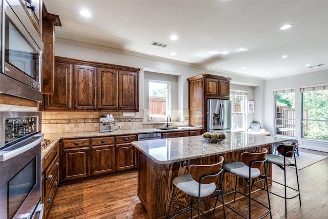 kitchen with stainless steel appliances, a center island, sink, and light stone countertops