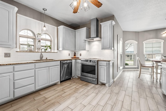 kitchen with wall chimney exhaust hood, sink, ceiling fan, stainless steel appliances, and white cabinets