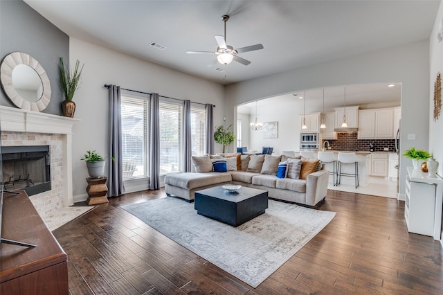 living room with a tiled fireplace, ceiling fan with notable chandelier, and dark wood-type flooring