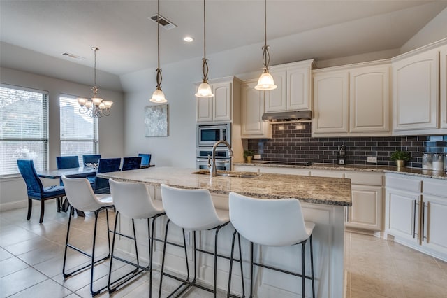 kitchen with pendant lighting, stainless steel microwave, sink, a center island with sink, and black electric cooktop