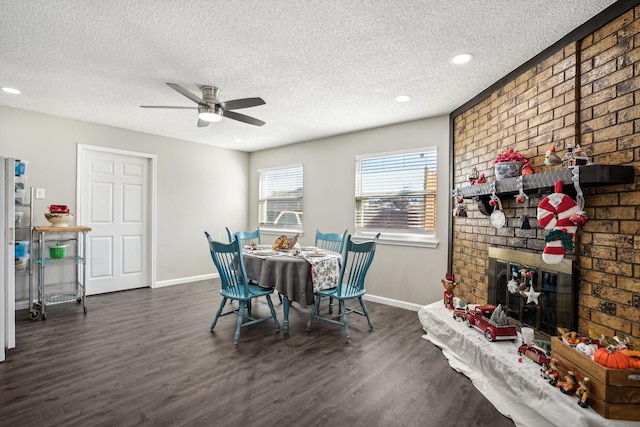 dining space with dark wood-type flooring, ceiling fan, a brick fireplace, and a textured ceiling