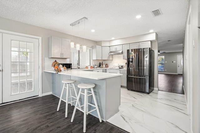 kitchen featuring a breakfast bar, hanging light fixtures, stainless steel fridge, kitchen peninsula, and white range with electric stovetop