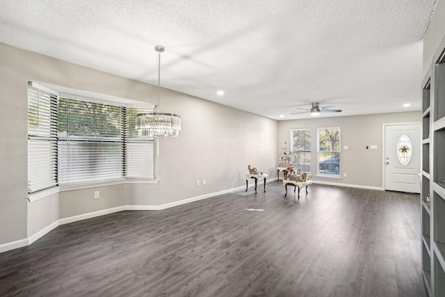 unfurnished dining area featuring dark hardwood / wood-style flooring, ceiling fan with notable chandelier, and a textured ceiling