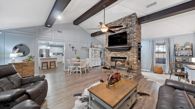 living room with wood-type flooring, high vaulted ceiling, a brick fireplace, ceiling fan, and beam ceiling